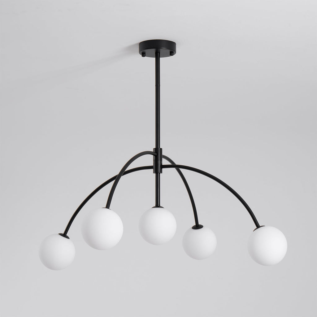 This black Clérachic chandelier has five white globes on arched arms hanging from a short rod, switched off, on a pale grey backdrop.