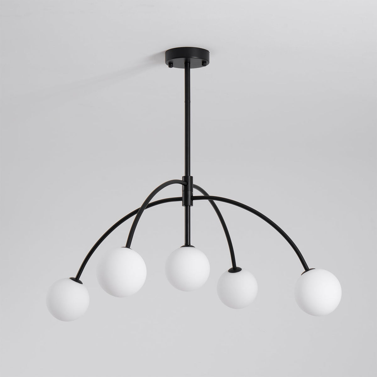 This black Clérachic chandelier has five white globes on arched arms hanging from a short rod, switched off, on a pale grey backdrop.