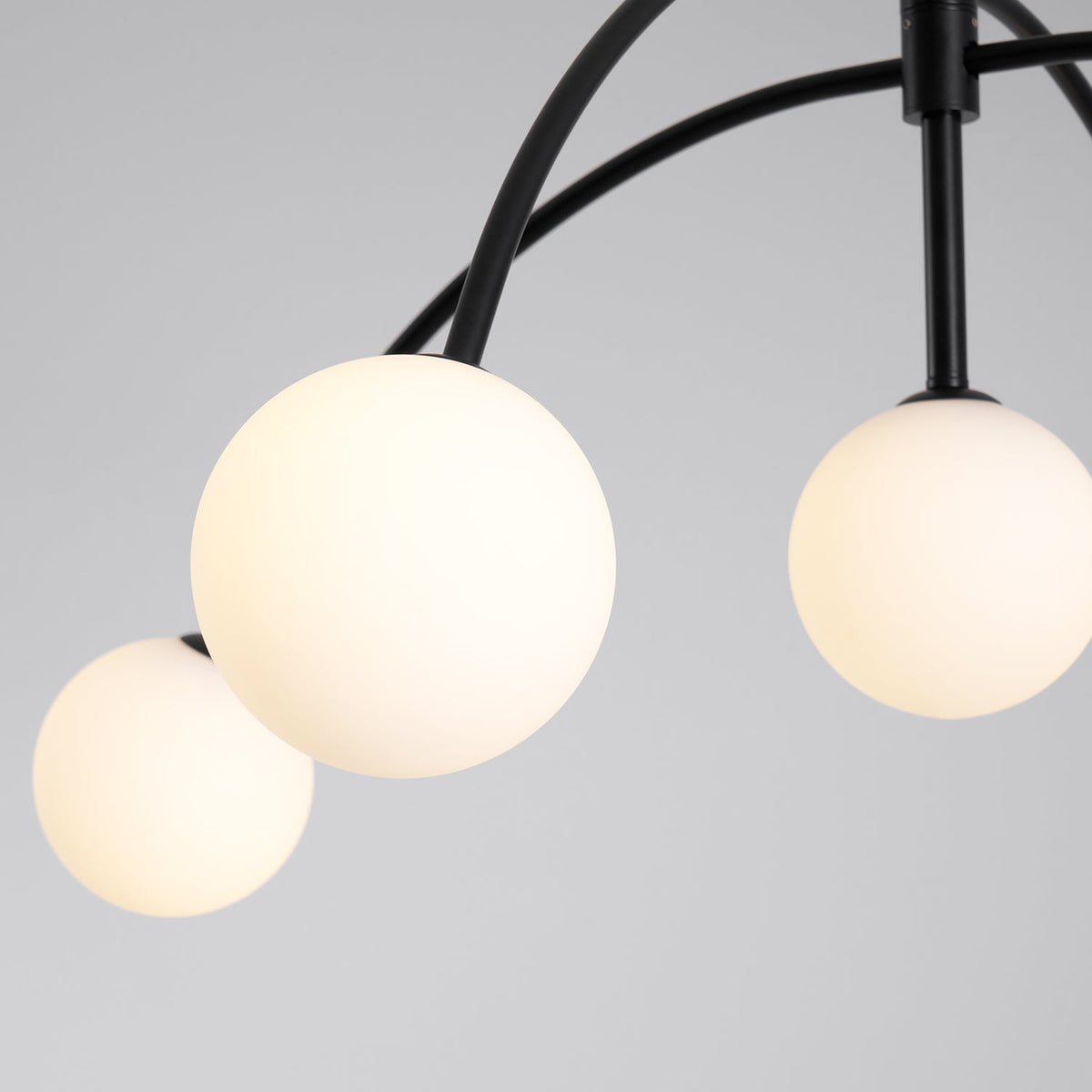Close view of three lit, frosted globes on this Clérachic chandelier, with a warm glow and black arms curving above them.