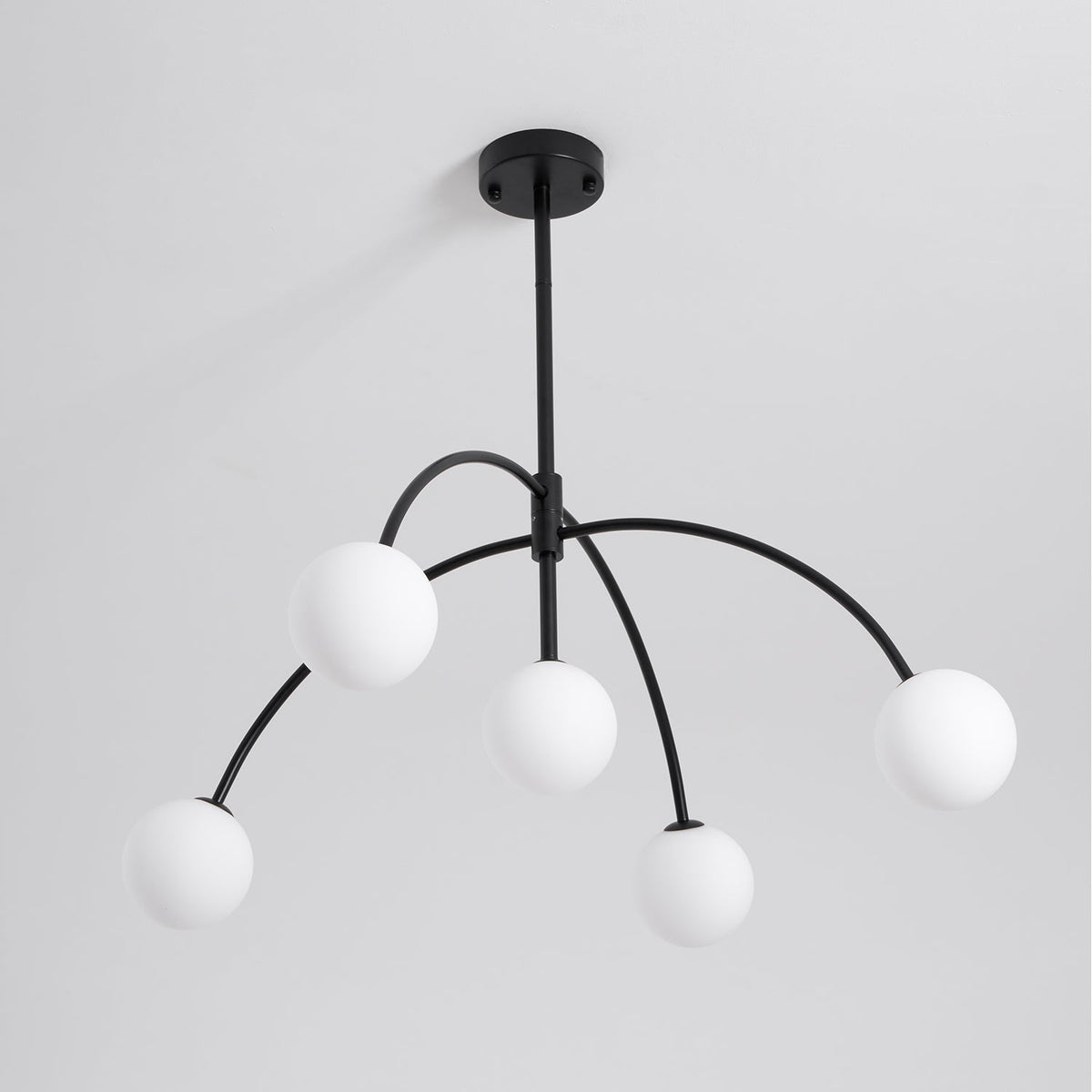This Clérachic chandelier, switched off, has five white globes on arched black arms under a round ceiling canopy, on pale grey.