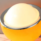 Close view of the white glass dome, polished chrome rim and glossy amber-yellow body of this Clérachic table lamp, glowing from within.