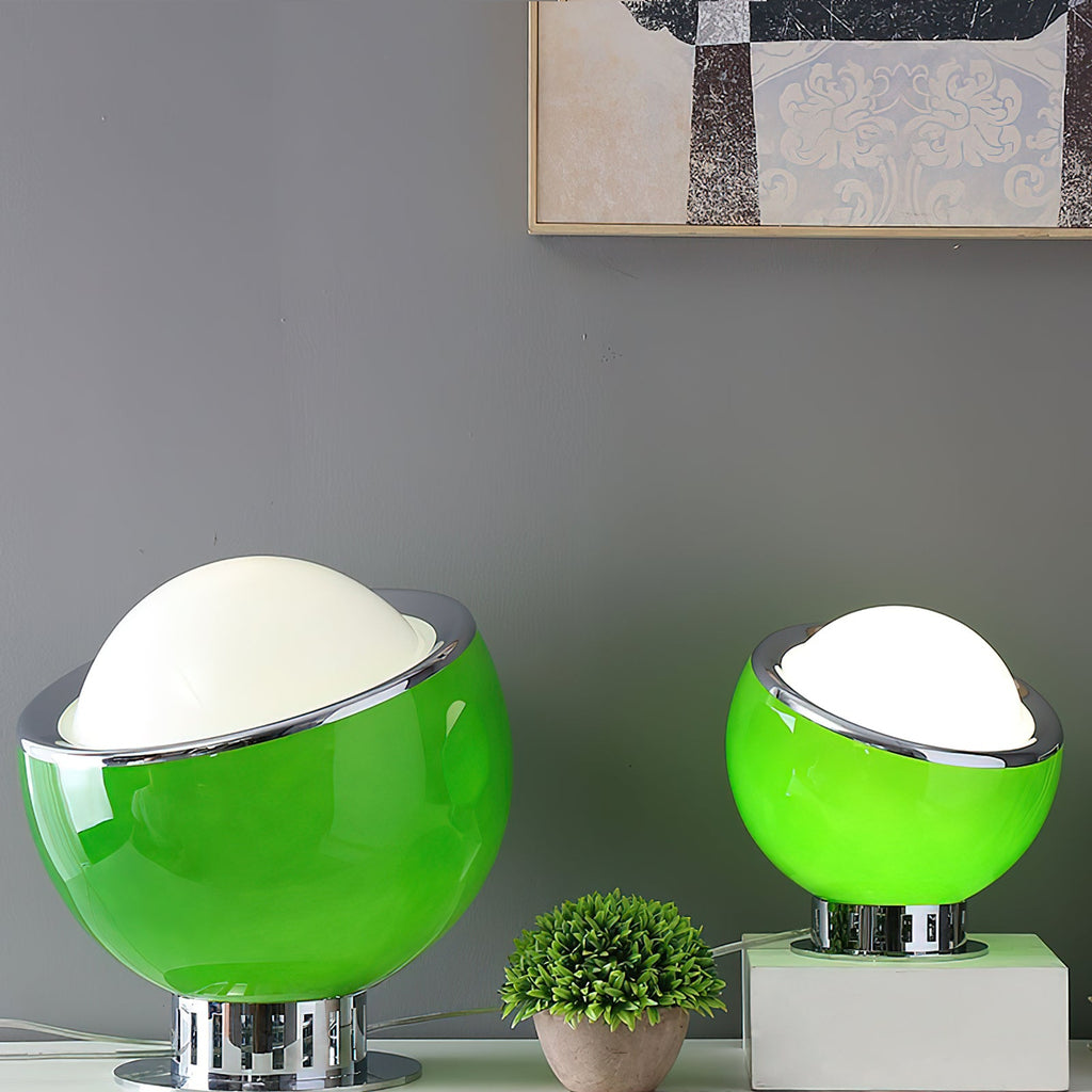 Two green Clérachic table lamps, large and small, sit on a white sideboard with a plant, the white domes lit against a grey wall.