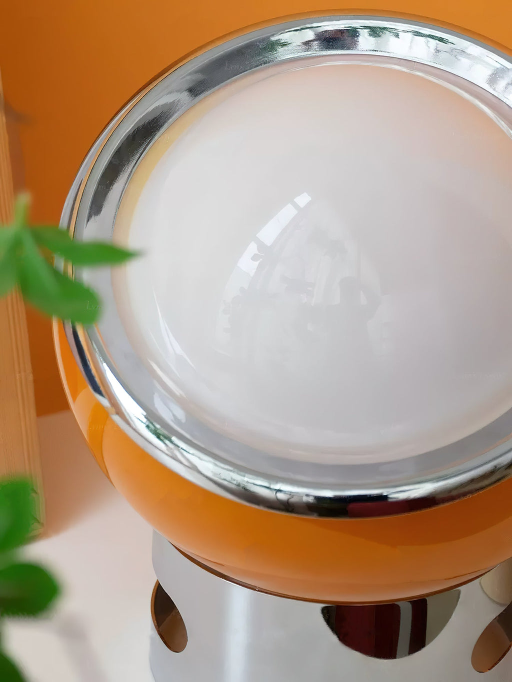 Close view of the glossy orange body, chrome rim and white dome of this Clérachic table lamp, with the cut-outs of the chrome stand just visible below.