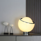 The lit white globe of this Clérachic table lamp sits on a dark console beside two bird figures, with a slatted panel behind it.