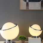 Two lit white globe lamps, one large and one small, stand on a plinth beside a plant under a framed print, from this Clérachic table lamp range.