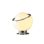 The smaller white version of this Clérachic table lamp, lit warm cream, with a tilted chrome rim and a ribbed chrome foot.
