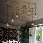 Warm light from nine bulbs on this Clérachic pendant falls across a grey bedroom with a quilted brown headboard and a tall palm by the window.