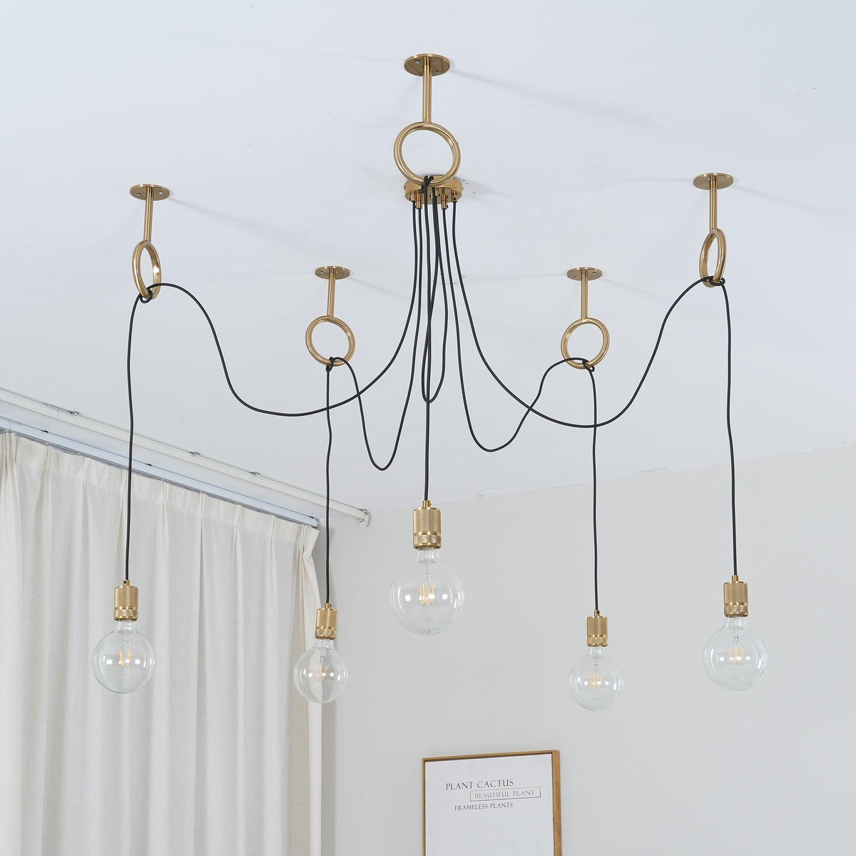 Looking up at five clear globe bulbs on black cables looped through copper rings, in front of a white curtain, on this Clérachic pendant.