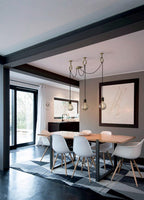 Three exposed bulbs of this Clérachic pendant hang above a dining table with white chairs, in an open room with black steel doors.