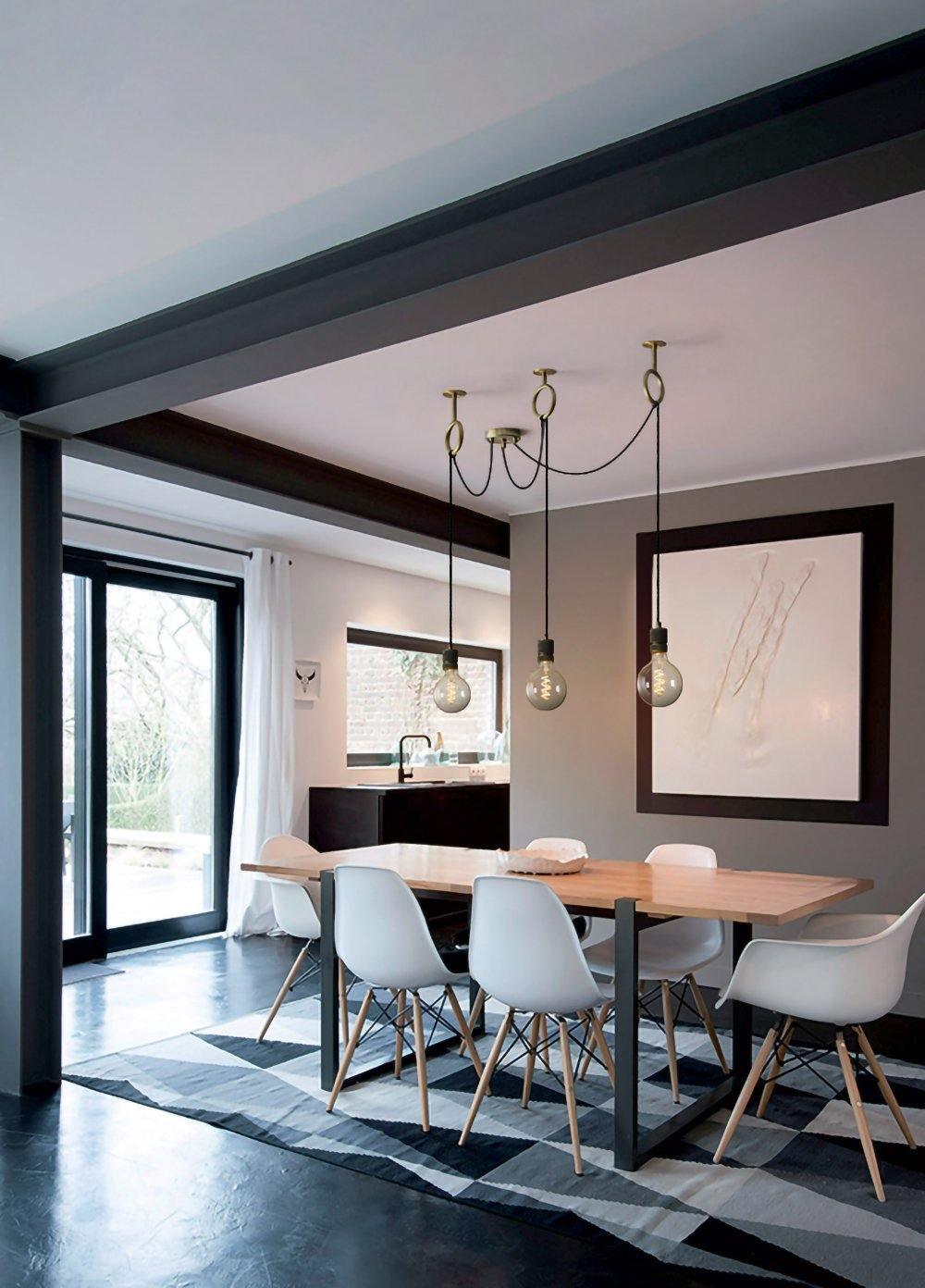 Three exposed bulbs of this Clérachic pendant hang above a dining table with white chairs, in an open room with black steel doors.