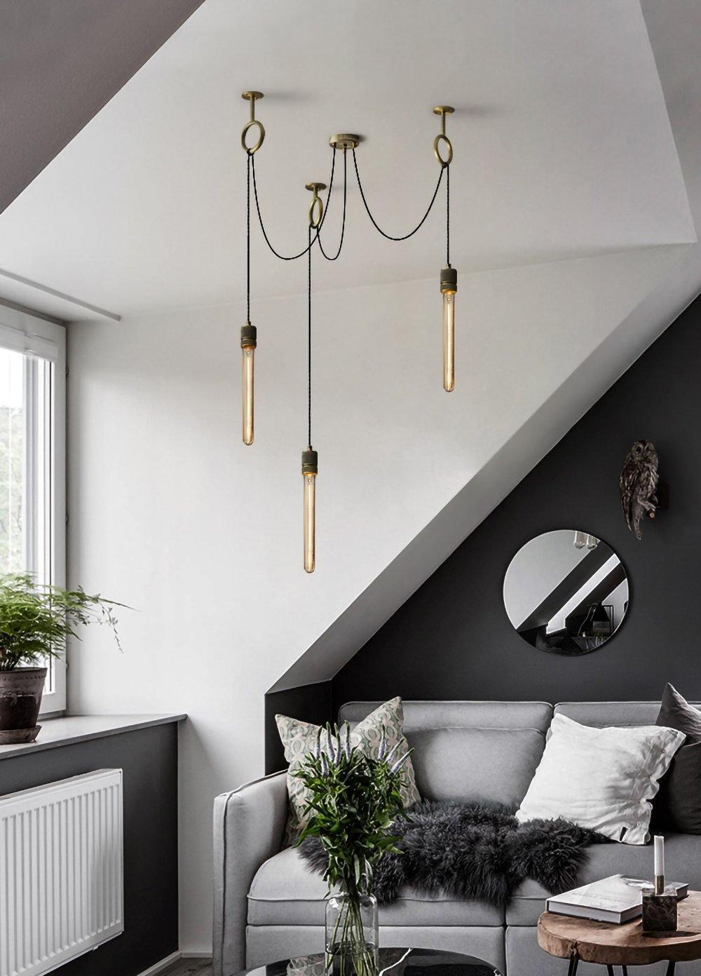 Three long tube bulbs hang at staggered heights from copper rings above a grey sofa under a sloped ceiling, with this Clérachic pendant.