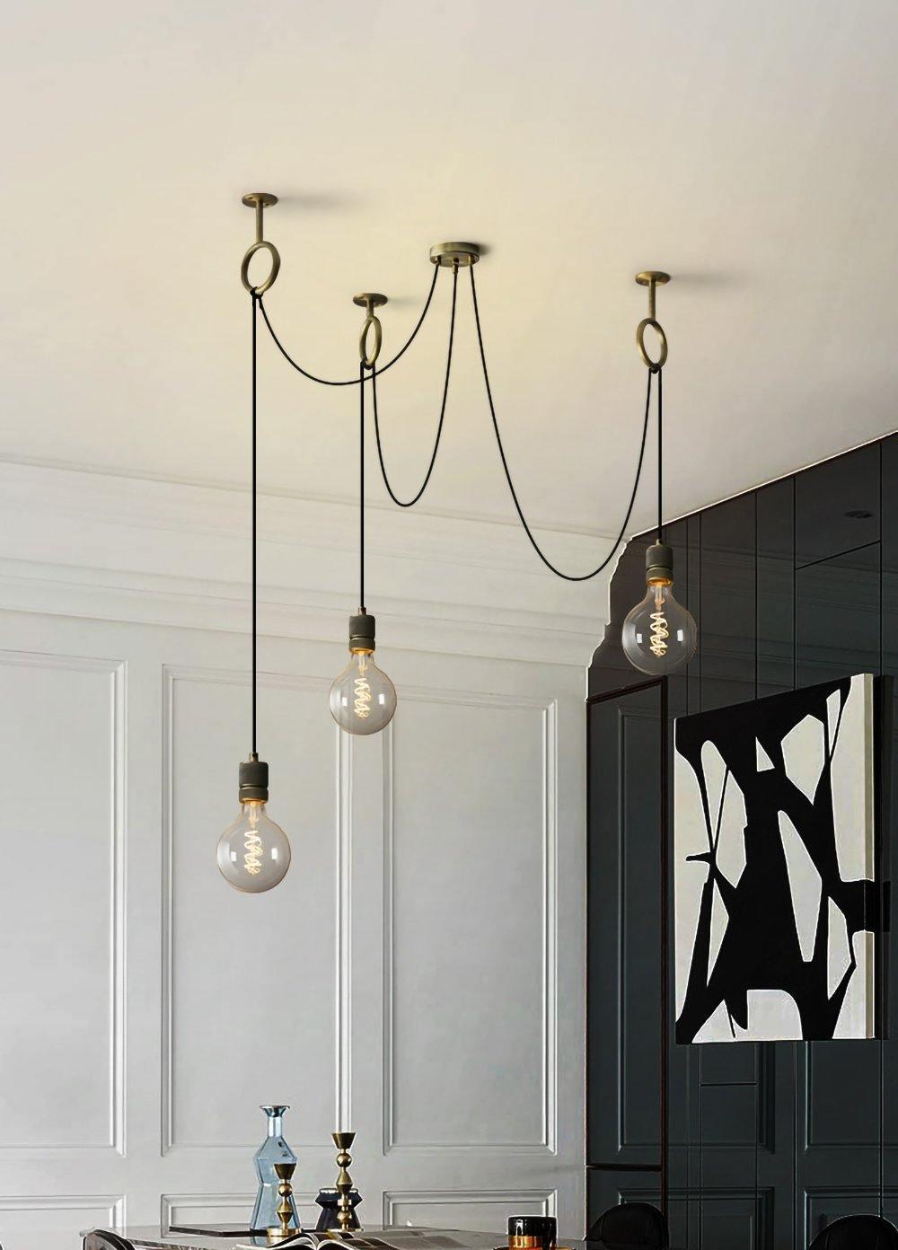 Three globe bulbs hang at different lengths from this Clérachic pendant in a white panelled room with a black-and-white painting.