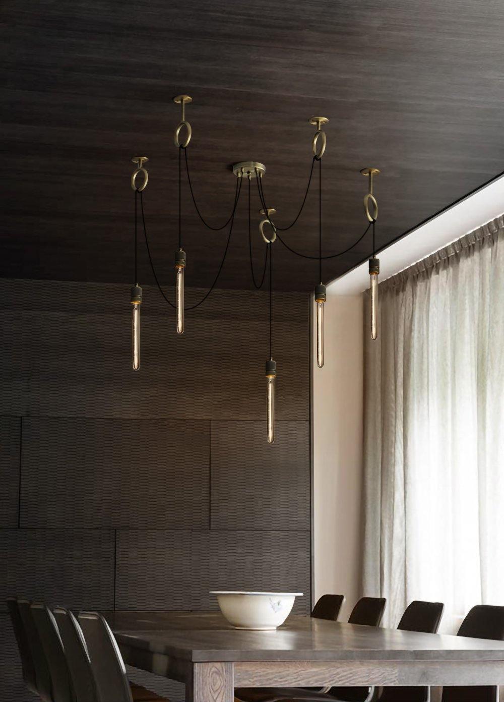 Seven slim tube bulbs hang on black cables from copper rings in a dark-panelled dining room, with this Clérachic pendant above a long table.