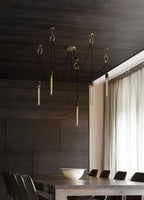 Seven slim tube bulbs hang on black cables from copper rings in a dark-panelled dining room, with this Clérachic pendant above a long table.