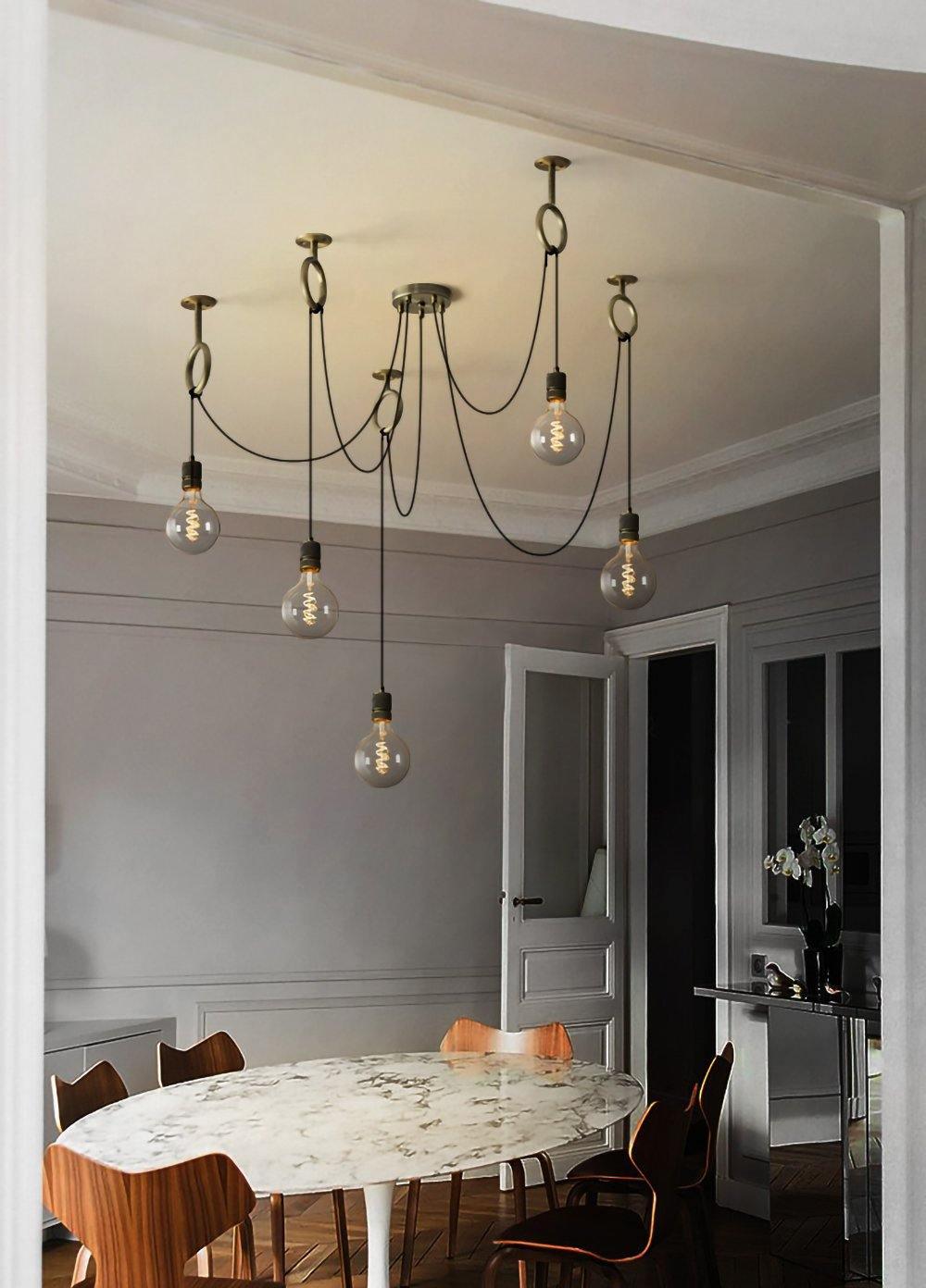 This Clérachic pendant hangs in a grey panelled room, its bulbs reaching down above an oval marble table and wooden chairs.