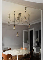 This Clérachic pendant hangs in a grey panelled room, its bulbs reaching down above an oval marble table and wooden chairs.