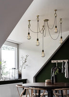 Globe bulbs of this Clérachic pendant hang beneath a sloped white ceiling near a dark green wall and a round dark dining table.