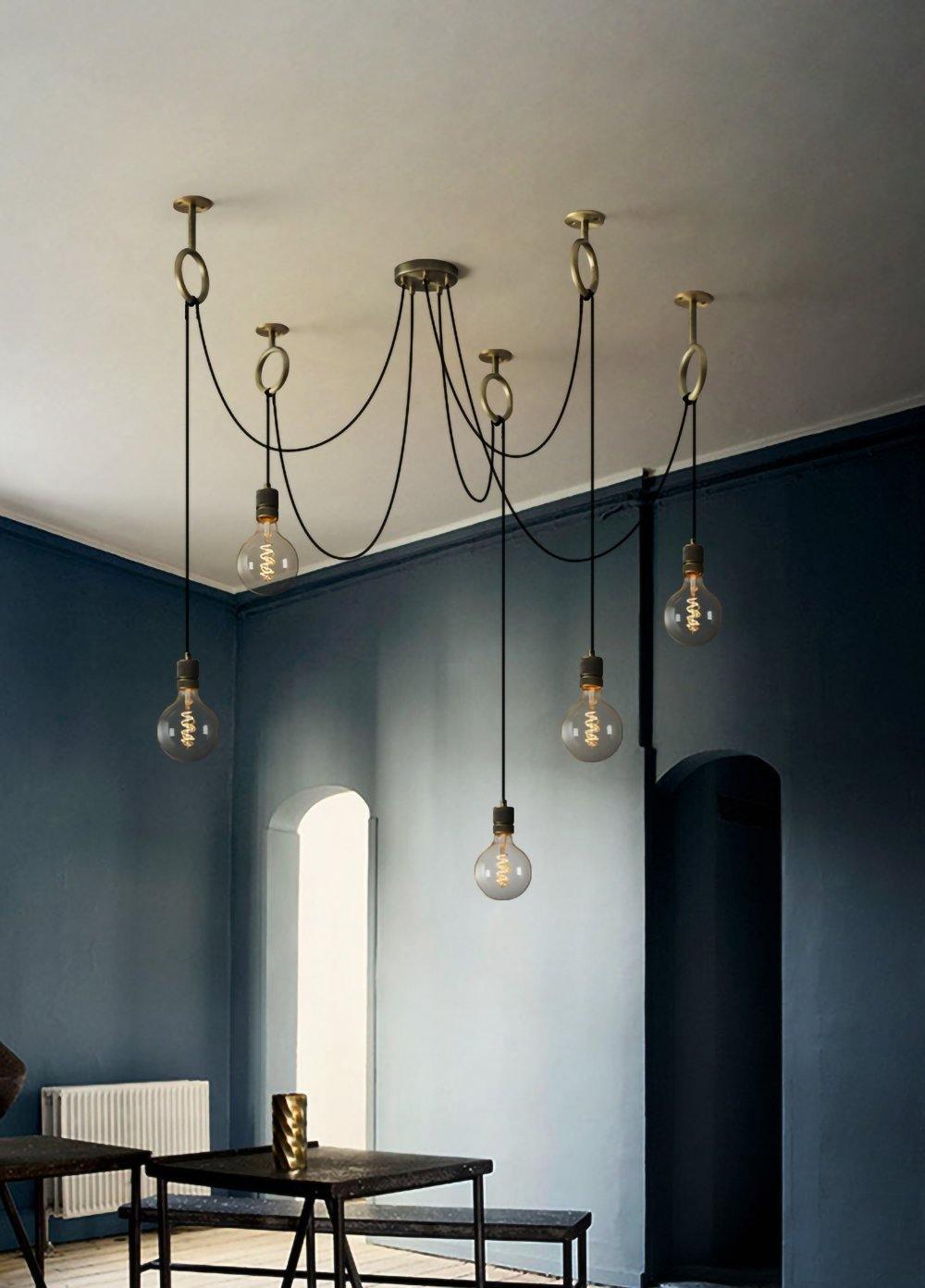 This Clérachic pendant hangs in a tall room with blue-grey walls and an arched door, its bulbs set above a black dining table.