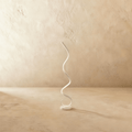Clérachic white spiral LED floor lamp, a single ribbon curling up from a round base, on a limewash floor and wall.