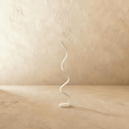 Clérachic white spiral LED floor lamp, a single ribbon curling up from a round base, on a limewash floor and wall.