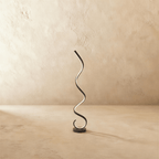 Clérachic black spiral LED floor lamp, a glowing ribbon rising in curves from a round black base against limewash.