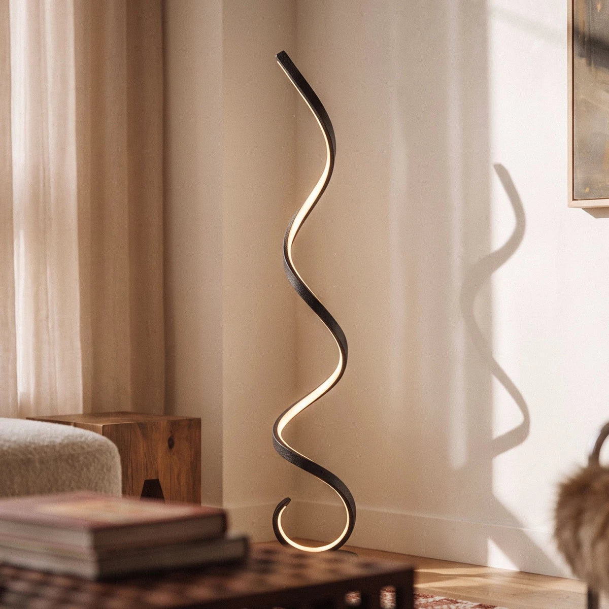 Clérachic black spiral floor lamp lit warm along its inner edge, casting a curving shadow on a sunlit wall.
