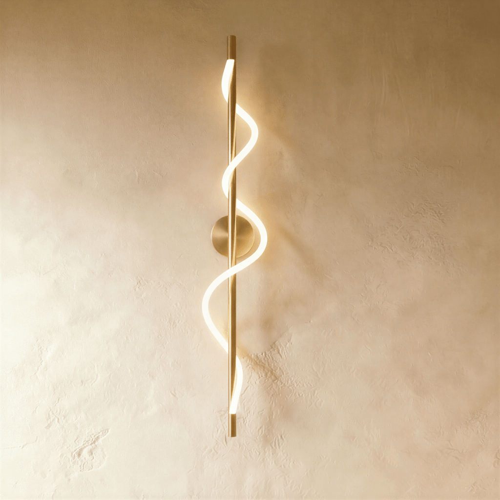 Clérachic slim vertical brass wall light with a glowing spiral LED strip winding round its rod, on a warm limewash wall.