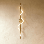 Clérachic slim vertical brass wall light with a glowing spiral LED strip winding round its rod, on a warm limewash wall.