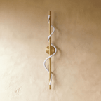 Clérachic brass vertical wall light with a round backplate and an unlit white spiral silicone strip, on a golden limewash wall.