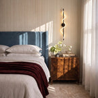 Clérachic black spiral LED wall light glowing above a burr-wood bedside cabinet, beside a blue headboard and striped wall.