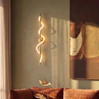 Clérachic brass spiral LED wall light glowing against a sage-green wall beside a large abstract painting and a rust sofa.