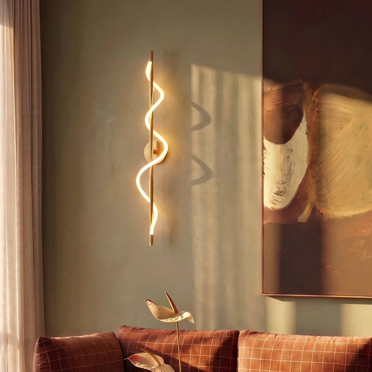 Clérachic brass spiral LED wall light glowing against a sage-green wall beside a large abstract painting and a rust sofa.
