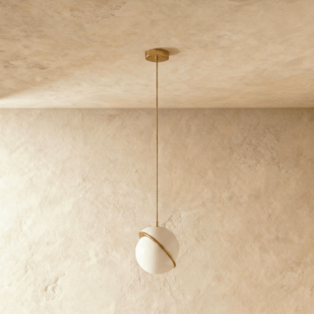 Clérachic opal white sphere pendant with a tilted brass-finish band, switched off on a brass rod and canopy against plaster.