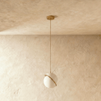 Clérachic opal white sphere pendant with a tilted brass-finish band, switched off on a brass rod and canopy against plaster.