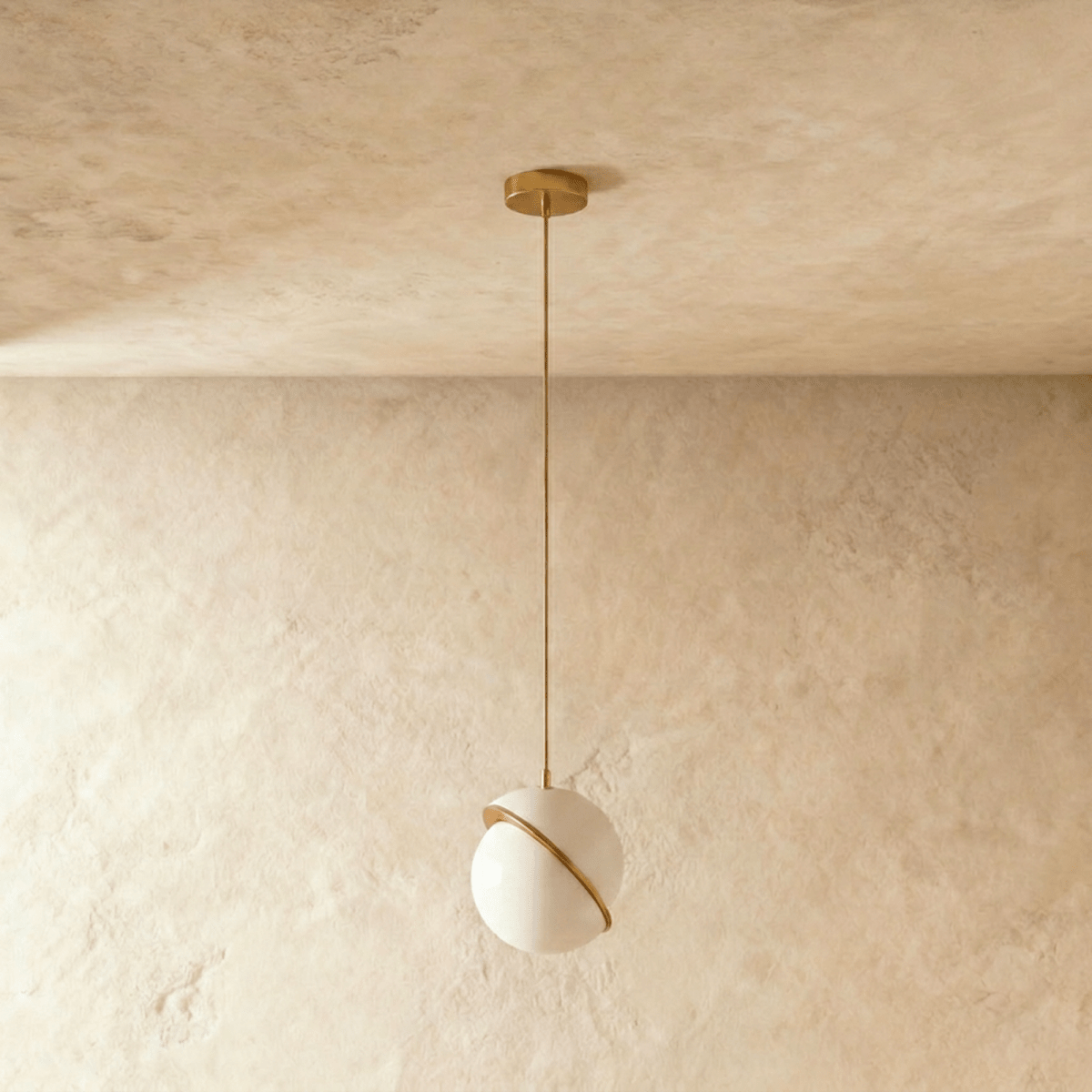 Clérachic opal white sphere pendant with a tilted brass-finish band, switched off on a brass rod and canopy against plaster.