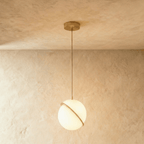 Clérachic largest opal white sphere pendant in the set, a tilted brass-finish ring across the globe, hung on a brass rod.