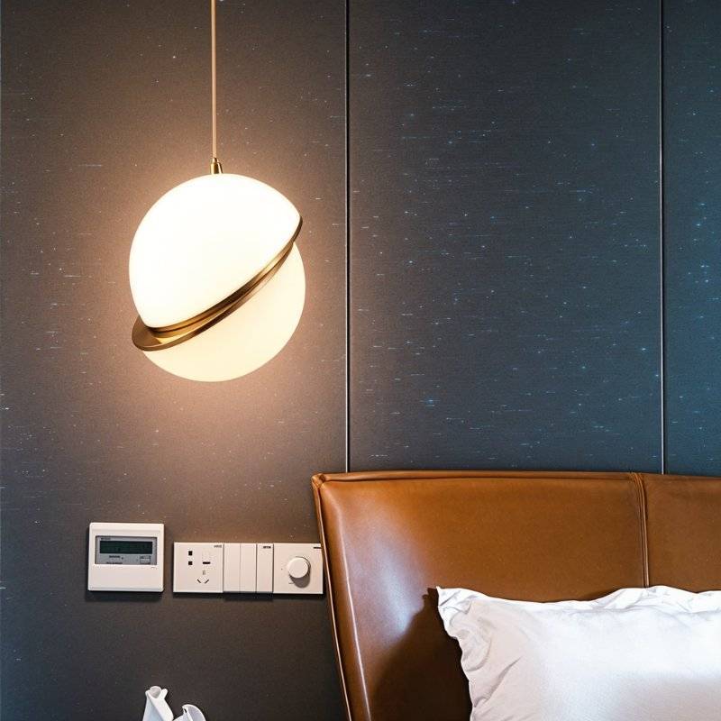 Clérachic opal white sphere pendant with a brass-finish ring glowing beside a tan leather headboard on a dark panelled wall.