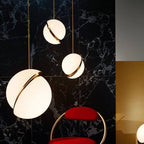 Three Clérachic opal white sphere pendants in different sizes against black marble tiles, with a red chair below.