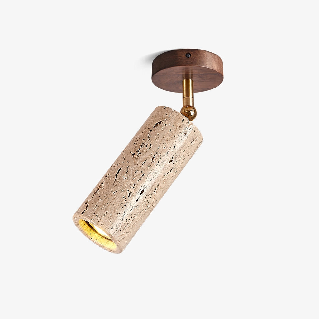 Travertine cylinder spotlight from Clérachic on a plain white backdrop, tilted on a brass pivot beneath a round walnut ceiling plate.