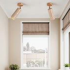 Two Clérachic travertine spotlights with light wood canopies on a white ceiling above a window with a woven roman blind.