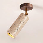 Close view of the walnut ceiling plate, brass pivot and pitted travertine cylinder on this Clérachic spotlight, lit at the open end.