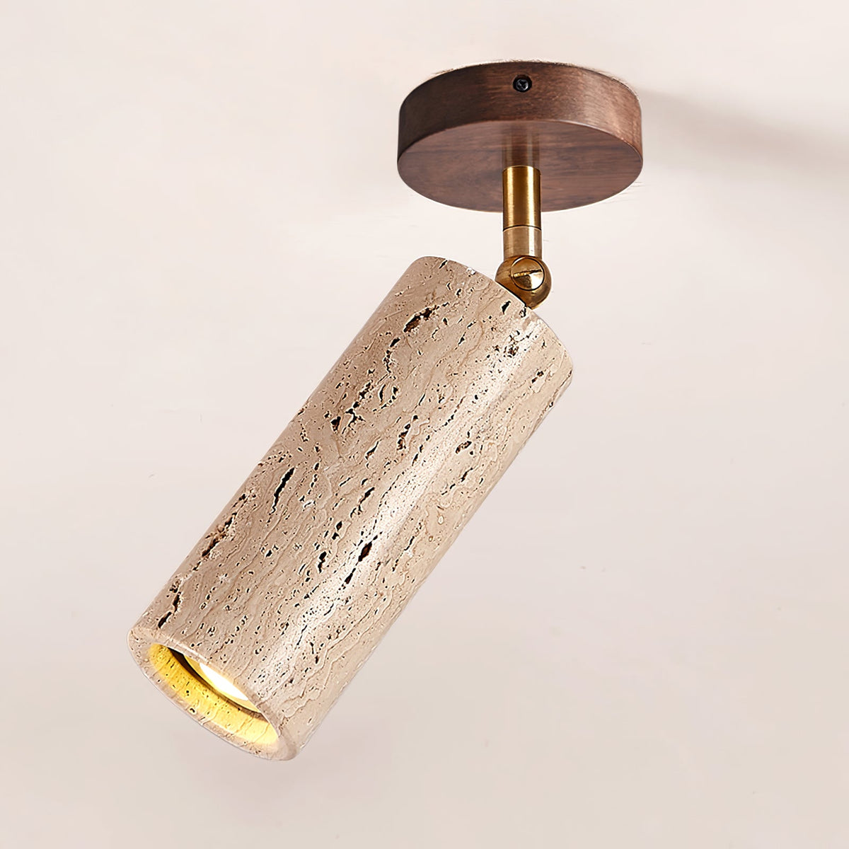 Close view of the walnut ceiling plate, brass pivot and pitted travertine cylinder on this Clérachic spotlight, lit at the open end.