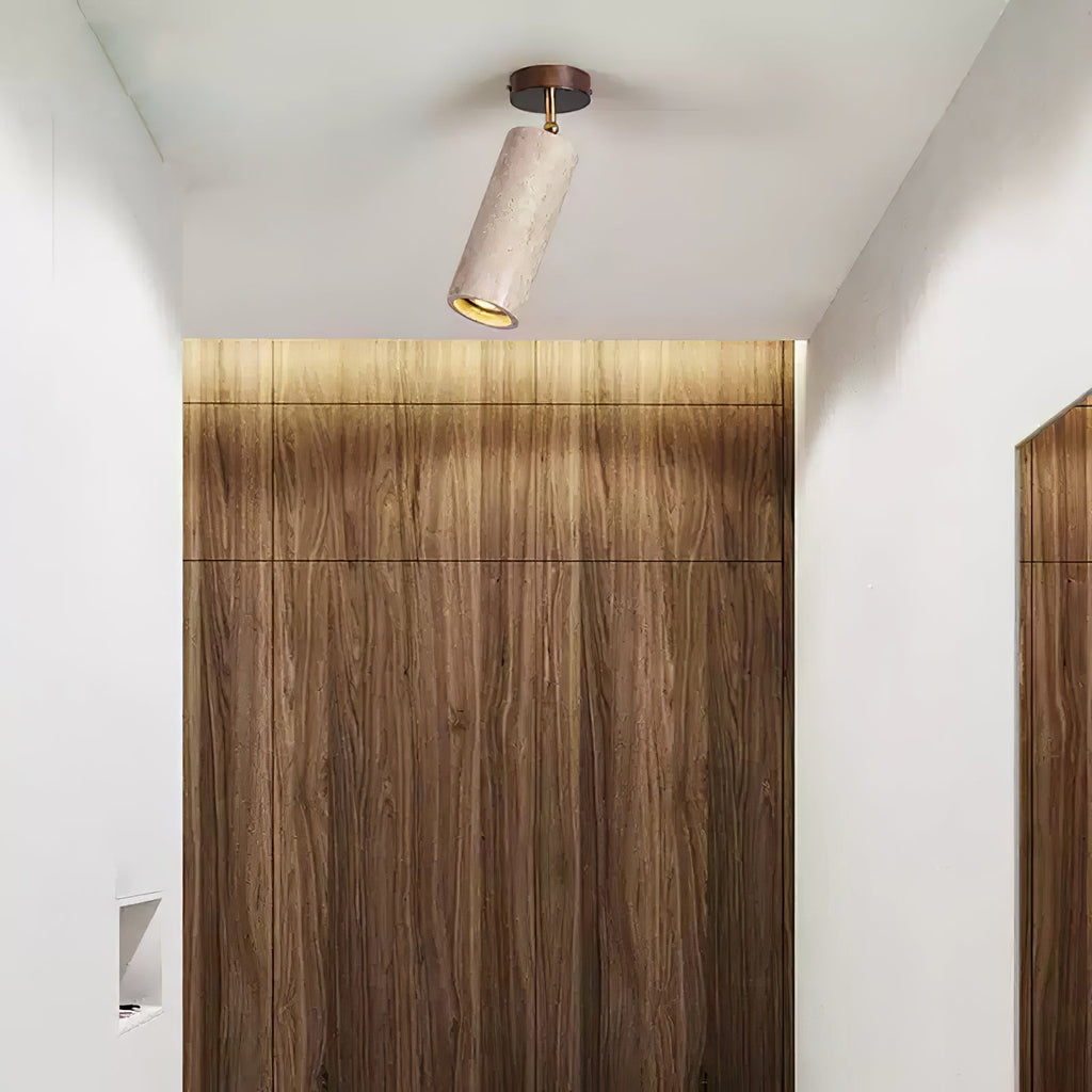 Clérachic travertine spotlight with a dark canopy tilted on a white ceiling, in front of a wood-grain panel lit from above.
