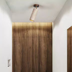 Clérachic travertine spotlight with a dark canopy tilted on a white ceiling, in front of a wood-grain panel lit from above.