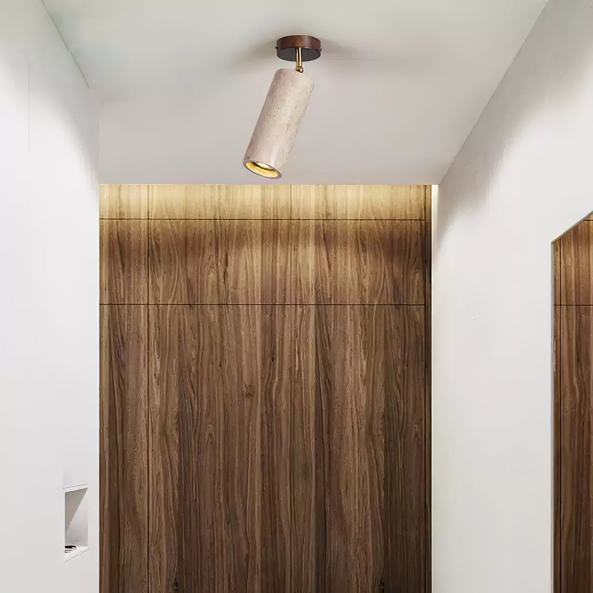 Clérachic travertine spotlight with a dark canopy tilted on a white ceiling, in front of a wood-grain panel lit from above.