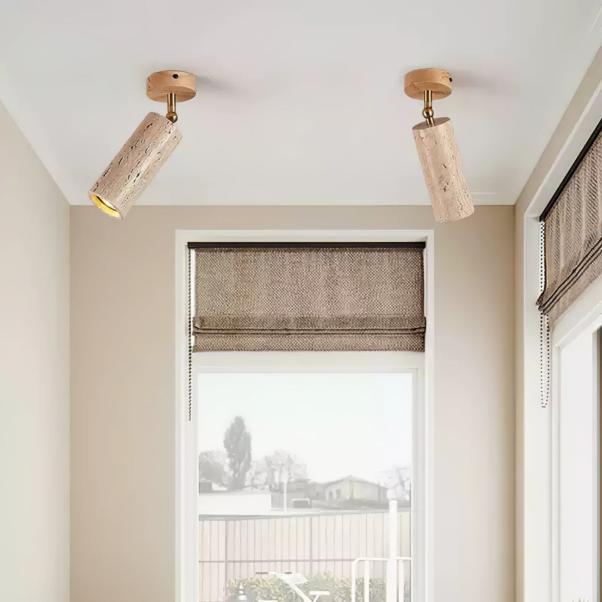 Pair of Clérachic travertine spotlights on a white ceiling, pivoted to face different ways above a window with a woven blind.