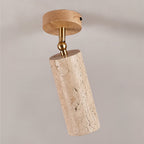 Close view of this Clérachic spotlight on a grey ceiling, with a pale wood canopy, a brass ball joint and a pitted travertine cylinder.