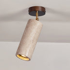 Clérachic travertine spotlight on a grey ceiling, a dark canopy above a brass pivot and a warm light inside the stone cylinder.