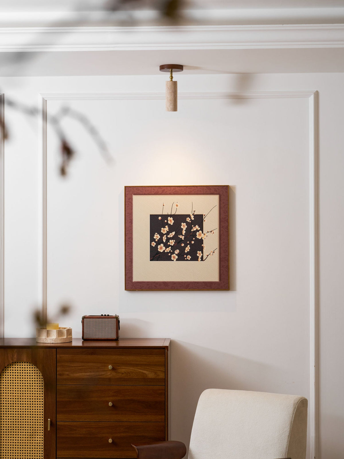 Small Clérachic travertine spotlight high on a white panelled wall above a framed blossom print and a walnut chest of drawers.