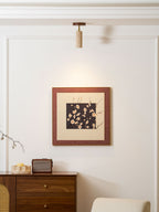 Clérachic stone spotlight on the ceiling above a framed blossom print, with a walnut sideboard with cane doors and a cream chair below.